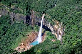 A breathtaking view of a tall waterfall cascading from a cliff into a turquoise pool, surrounded by lush green forest in Meghalaya, India.