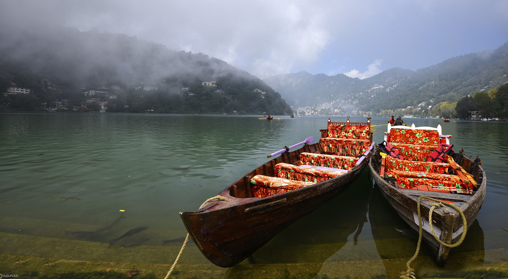 Two colorful wooden boats docked on the serene Naini Lake, surrounded by misty hills in Nainital.