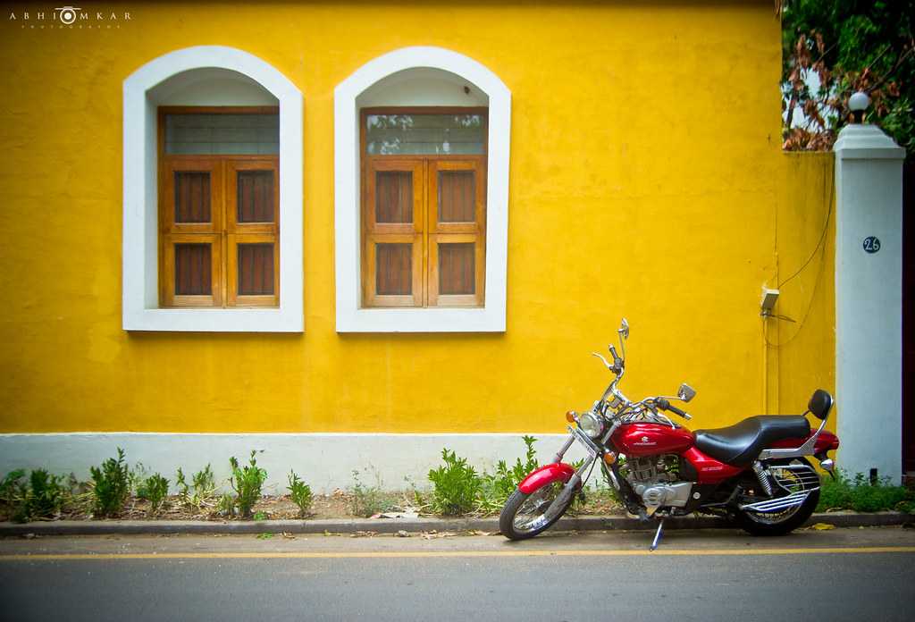 A vibrant yellow wall with classic wooden windows and a parked red motorcycle captures the charming streetscape of Pondicherry.